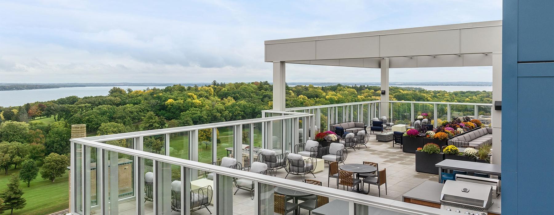 a deck with chairs and tables on it and with trees and a lake in the background