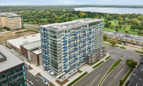 Aerial view of EO Madison Yards apartment building with lake and golf course backdrop
