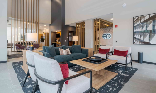 Modern apartment lobby lounge with EO branded sign, teal sofa, and wood slat dividers