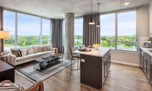 Open-concept one-bedroom living room and kitchen with panoramic lake and treetop views