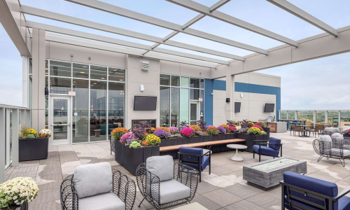 Apartment rooftop terrace with fire pit lounge, colorful flowers, and outdoor TVs