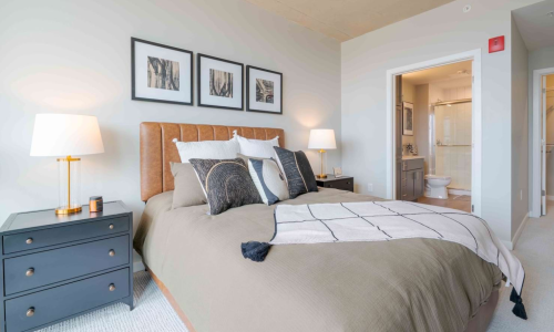 Primary bedroom with leather headboard, gold lamps, and en-suite bathroom doorway